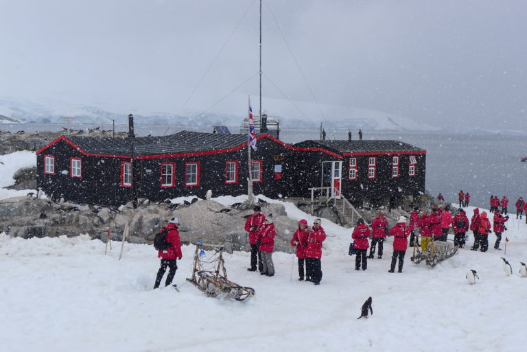 External view of Port Lockroy building with people, sledges and penguins